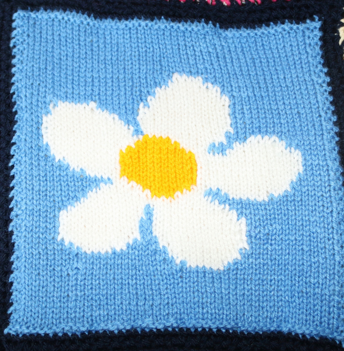 Knitted square of a large white flower on a pale blue background