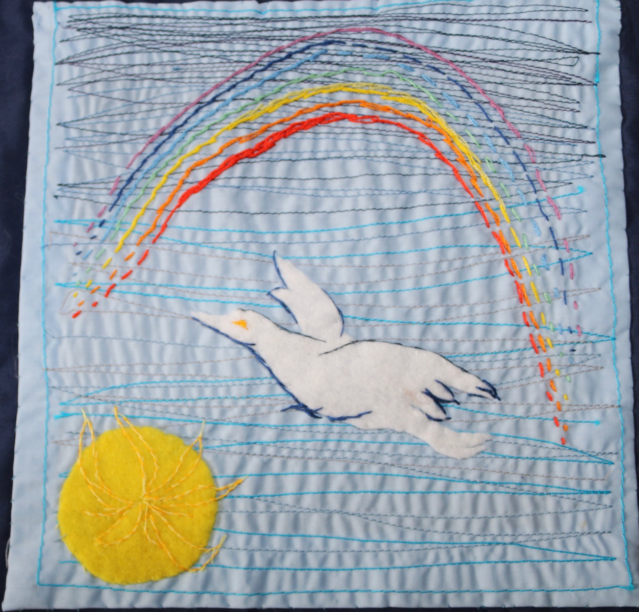 Image, created in embroidery, of a sun, dove and a rainbow