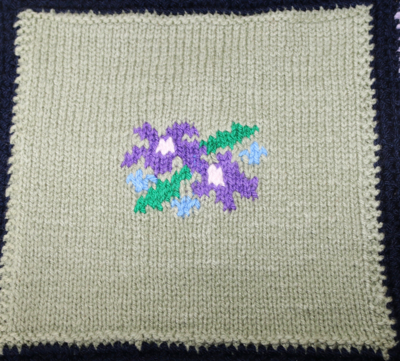 Knitted square with a spray of flowers in the middle, grey background