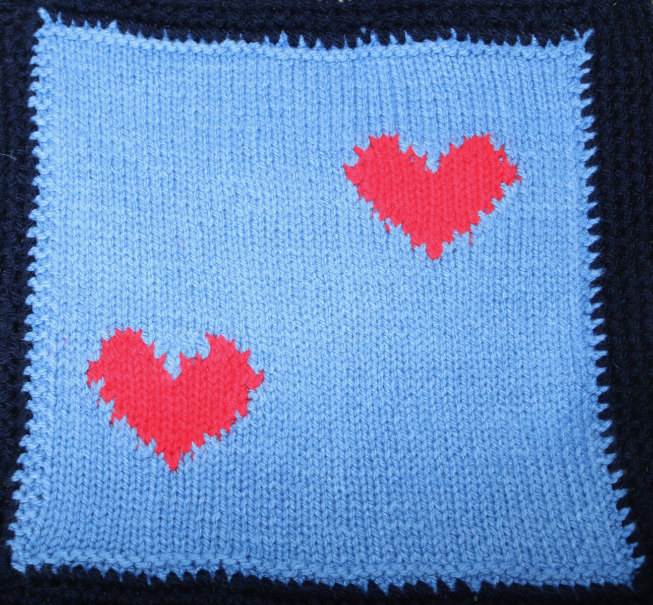 Knitted square: 2 red hearts on a pale blue background