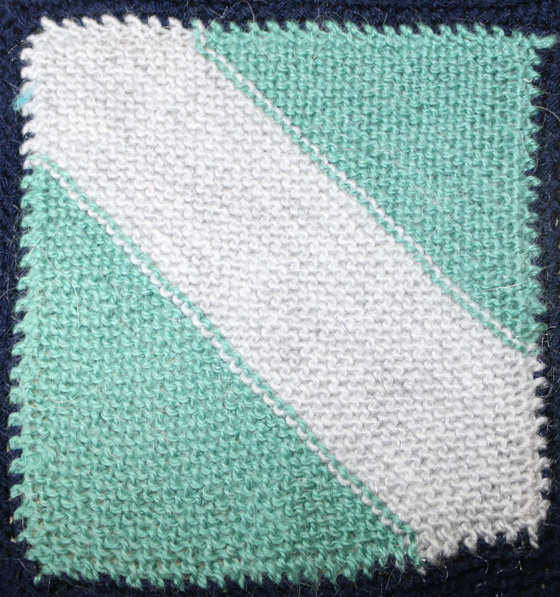 Knitted square: green background with white stripe running top left to bottom right