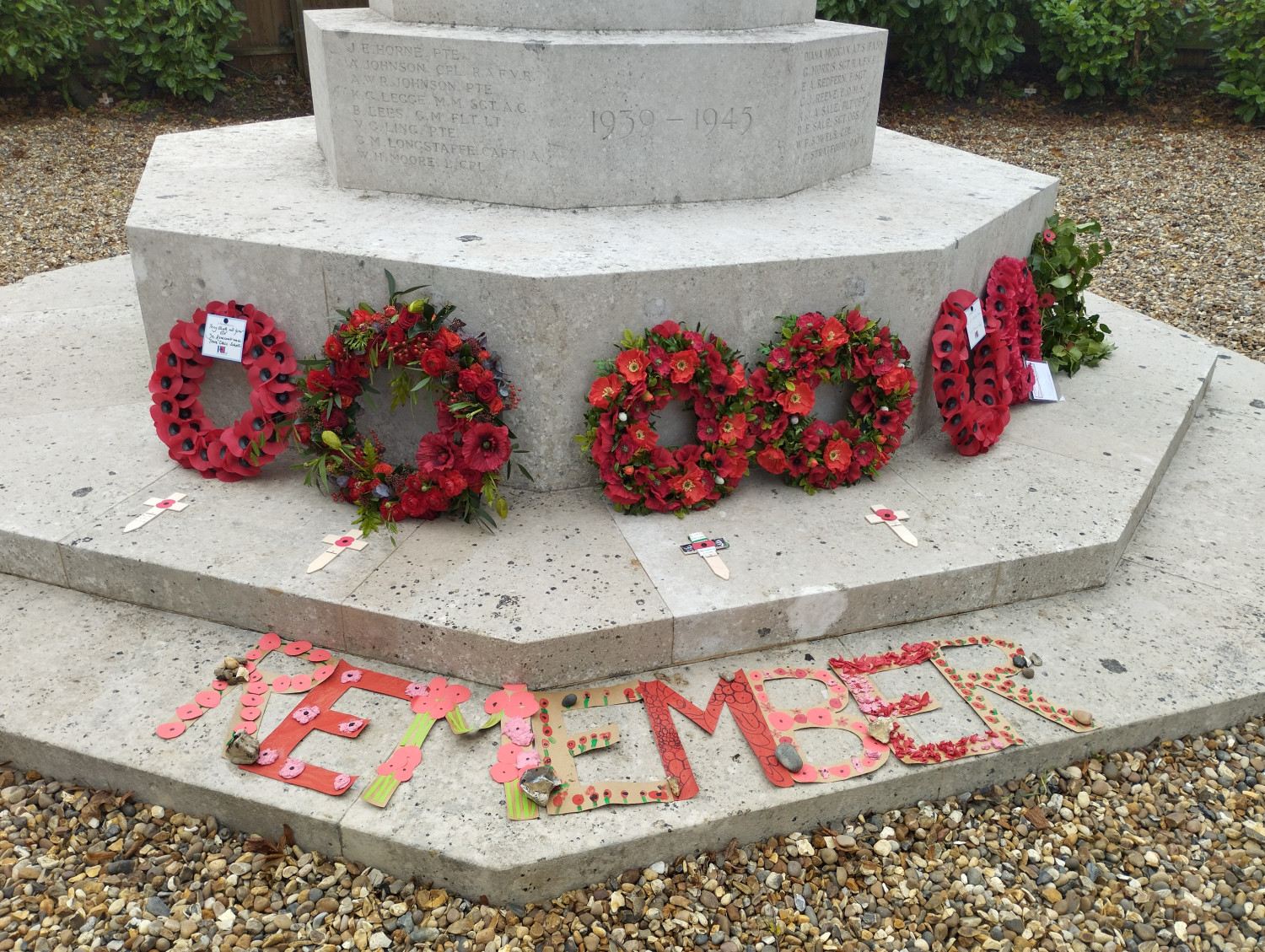 Image of 7 Poppy wreaths at foot of Eaton War Memorial taken by Patrick Richmond November 2022. The word Remember is spelt out in large card letters covered in poppy designs, made by local school children